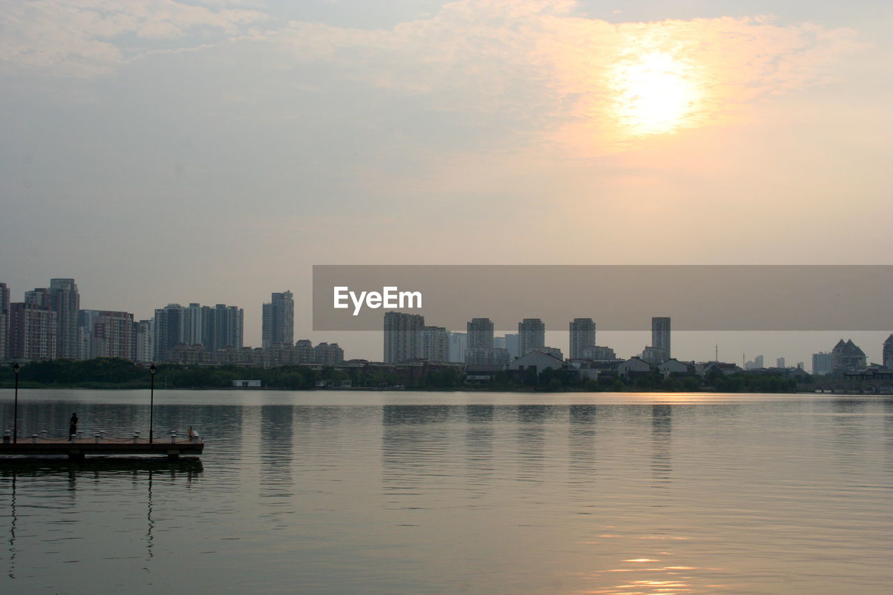 Sea by buildings against sky during sunset