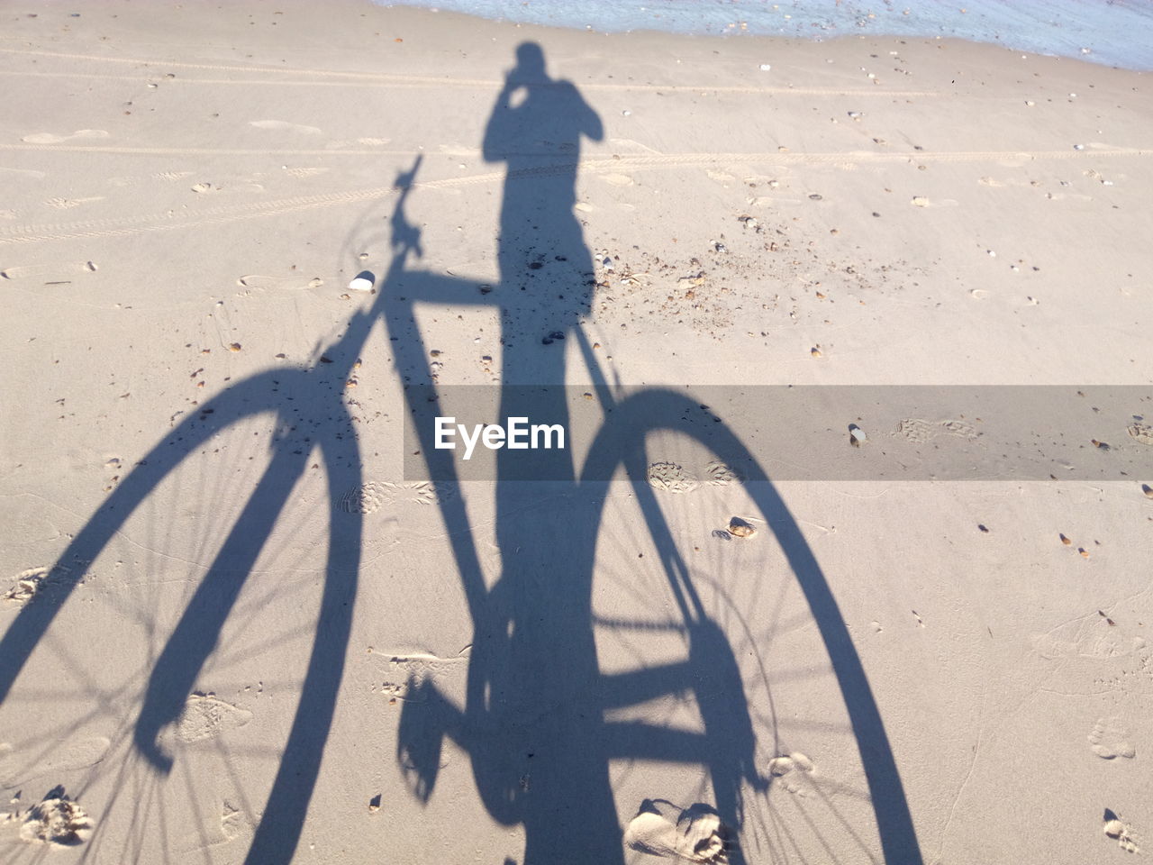 SHADOW OF MAN RIDING BICYCLE ON BEACH