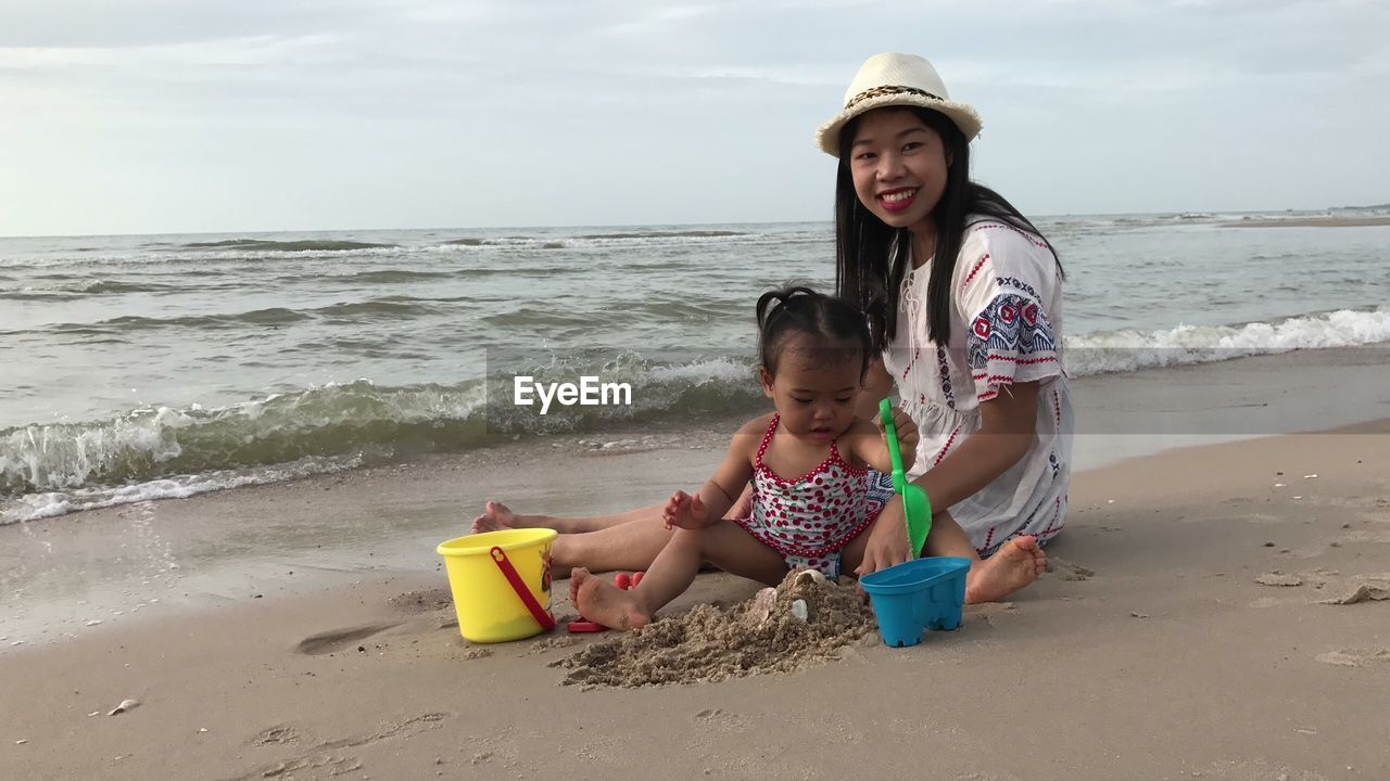 Smiling mother sitting with baby girl playing on shore at beach