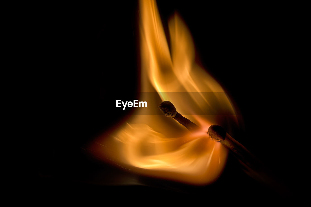 Close-up of burning matchstick over black background