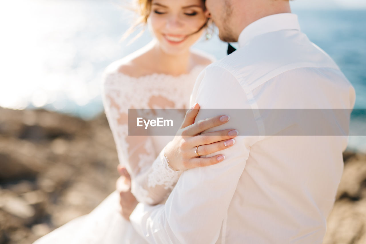 Midsection of bridegroom embracing against sea