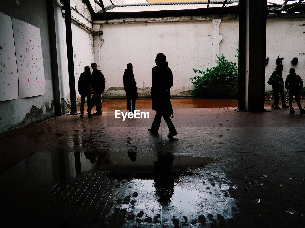 PEOPLE WALKING ON WET STREET AMIDST BUILDINGS