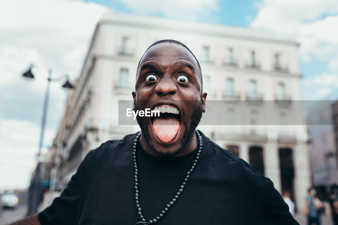 Portrait of cheerful black in urban scenery sticking out tongue and looking at camera