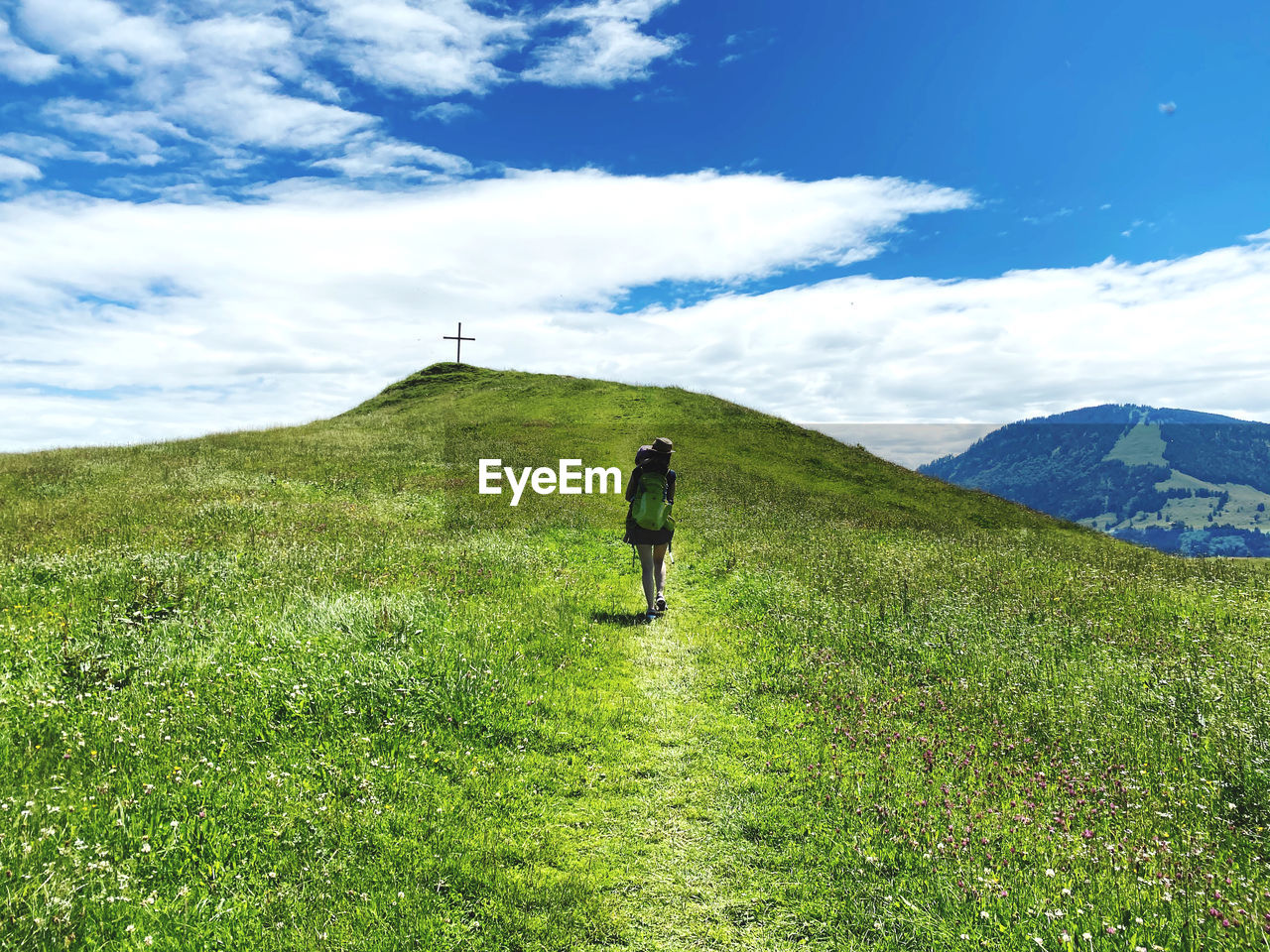 Rear view of woman walking up a grassy hill against mountains carrying child and backpack