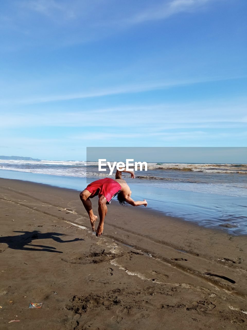 Young man jumping at beach against sky