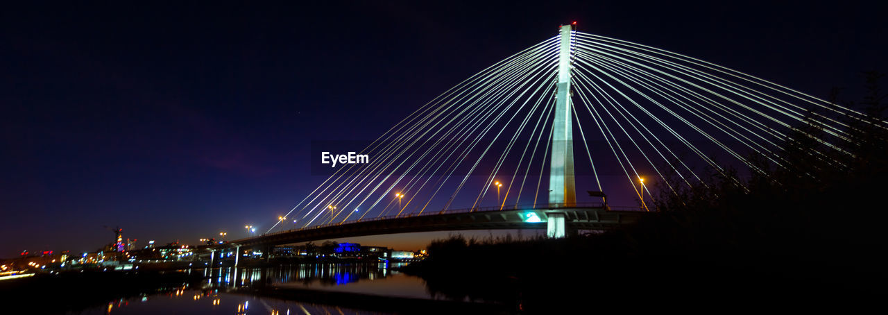ILLUMINATED BRIDGE ACROSS RIVER AT NIGHT