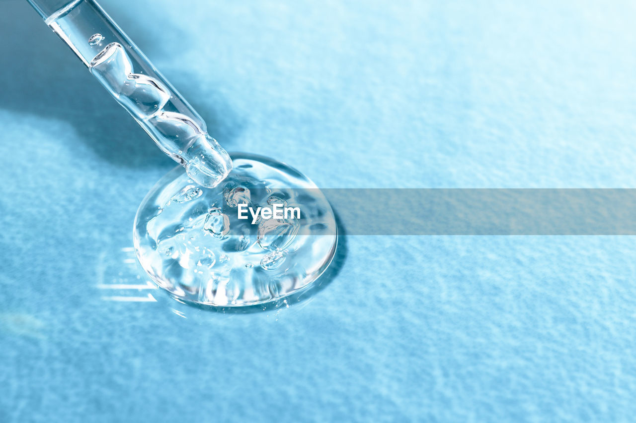 Glass pipette with acid for moisturizing the skin on a blue textural background close-up. 