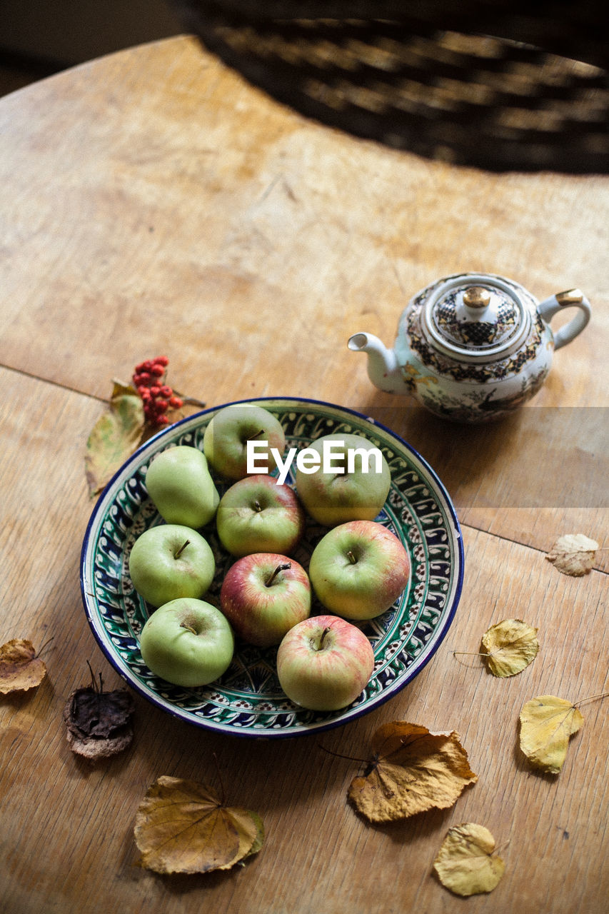 High angle view of apples in plate with dry leaves on wooden table