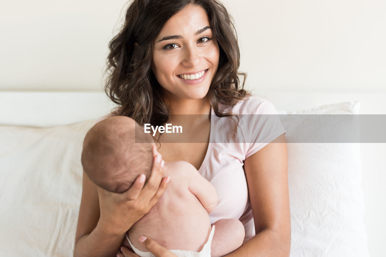Portrait of smiling mother carrying daughter on bed