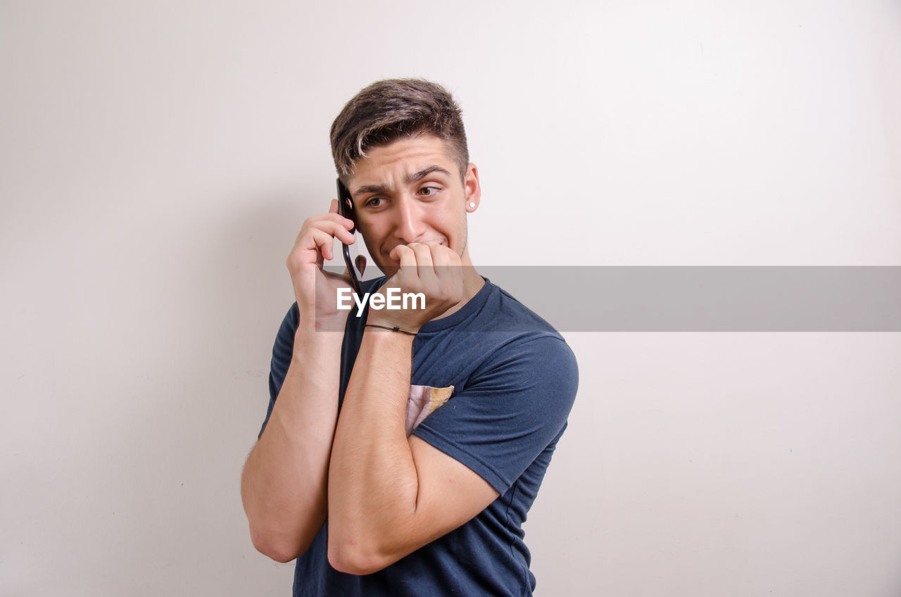 YOUNG MAN USING MOBILE PHONE AGAINST WALL