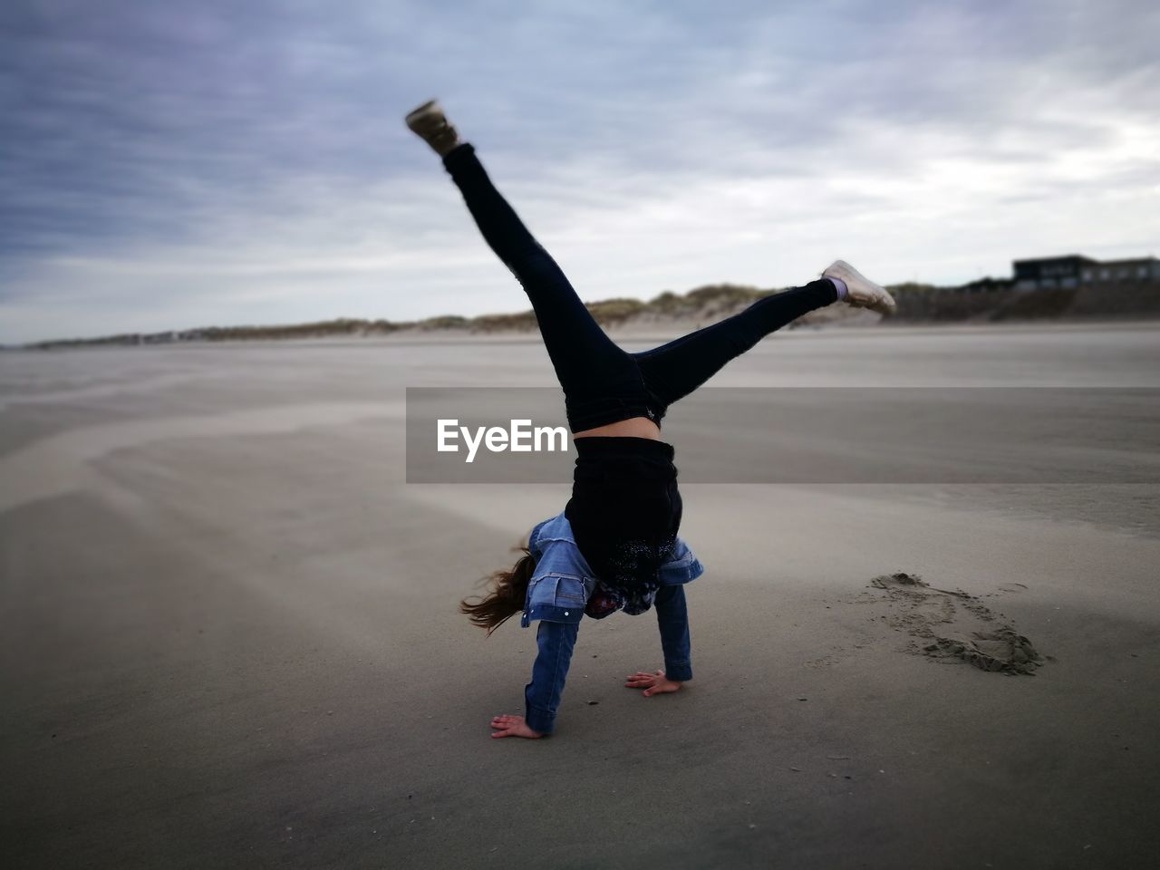 Full length of girl practicing handstand at beach against sky