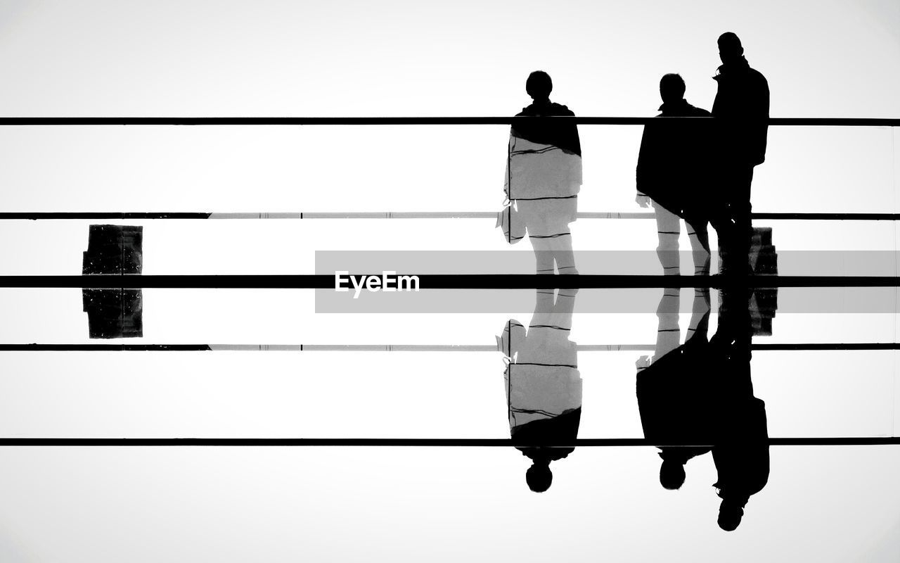 Digital composite image of silhouette men standing at railing against sky
