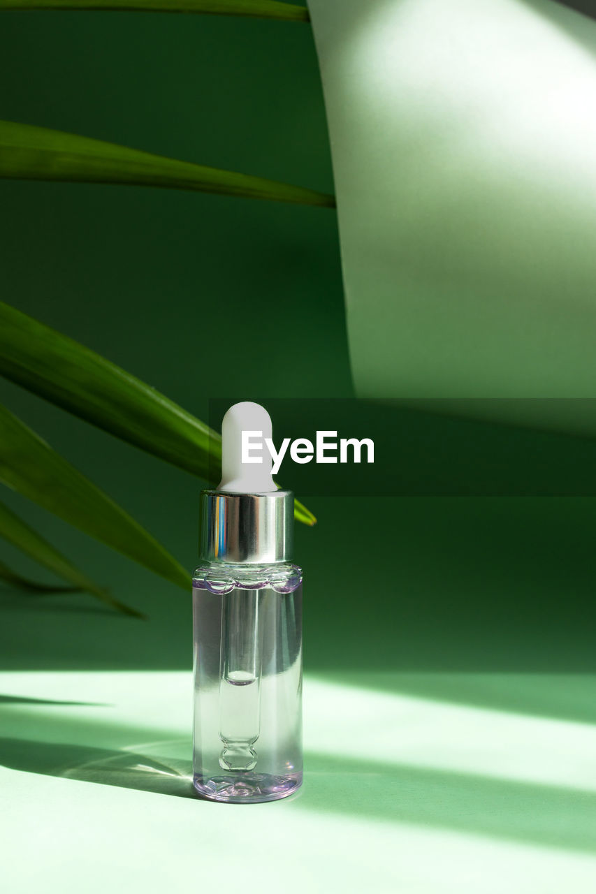 Transparent cosmetic bottle with a pipette in the rays of the bright sun on a green background