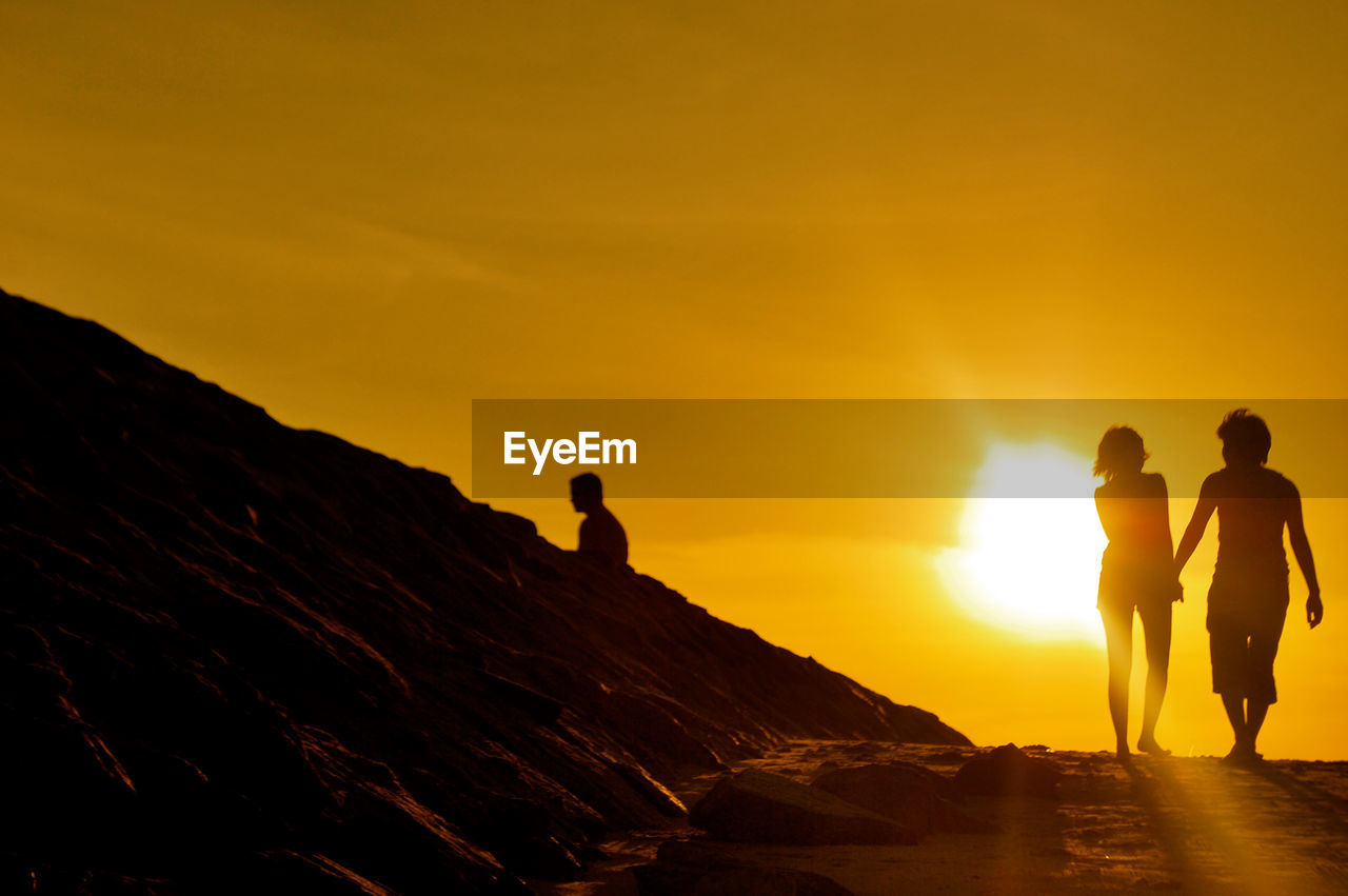 Silhouette of people standing on rock against sky during sunset