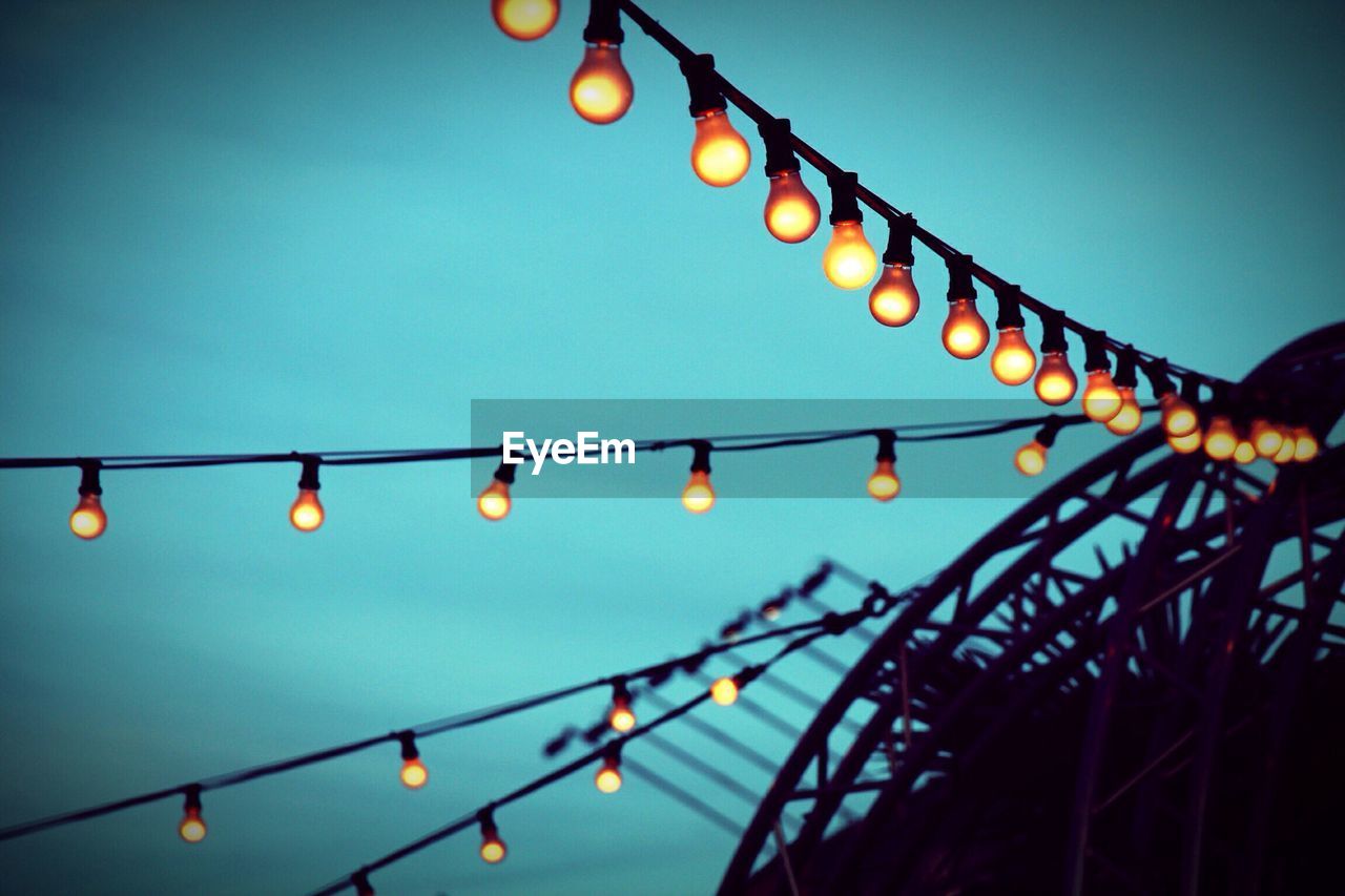 Low angle view of illuminated light bulbs hanging against sky