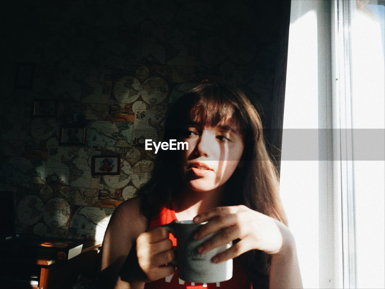 Thoughtful young woman holding coffee cup by window at home