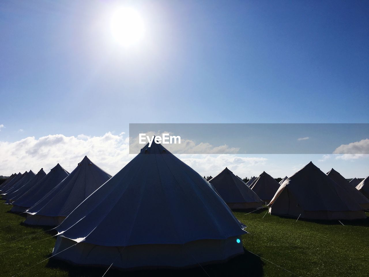 Tents on landscape against blue sky during sunny day
