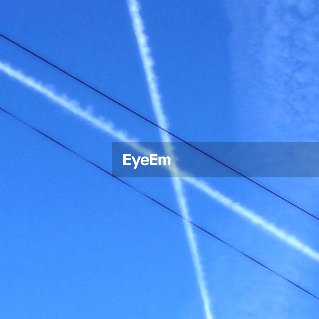 Low angle view of vapor trail and cables against sky