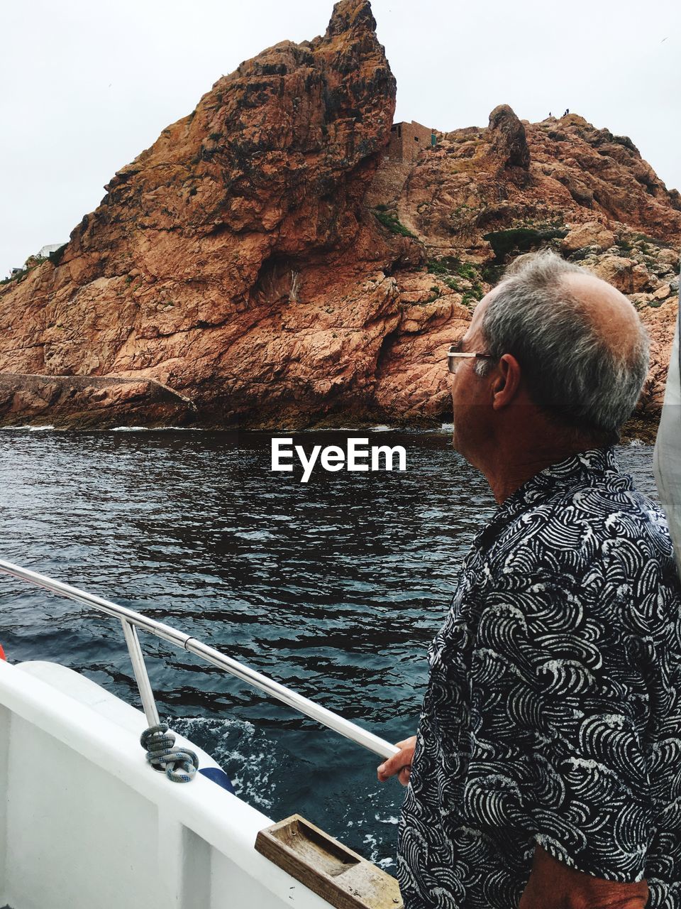 Side view of mature man standing on boat sailing against rock formations