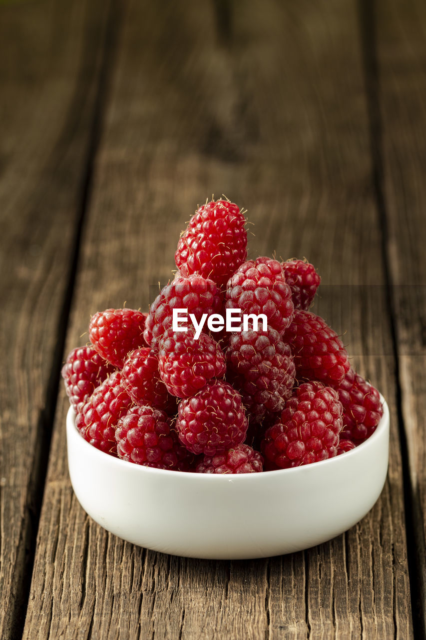 Fresh ripe raspberries in a white ceramic bowl on a dark brown wooden table with space for text