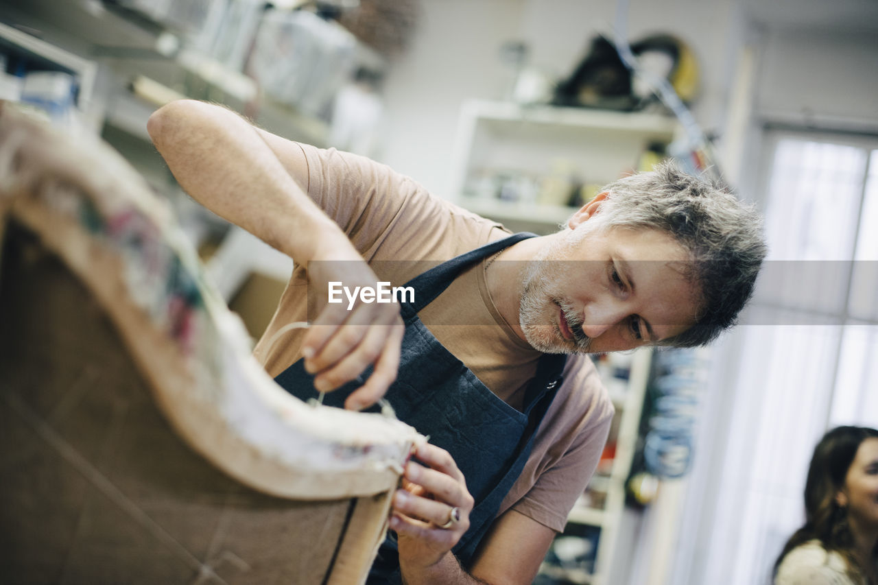 Mature craftsperson stitching furniture in workshop