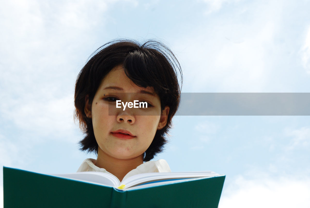 Low angle view of woman reading diary against sky