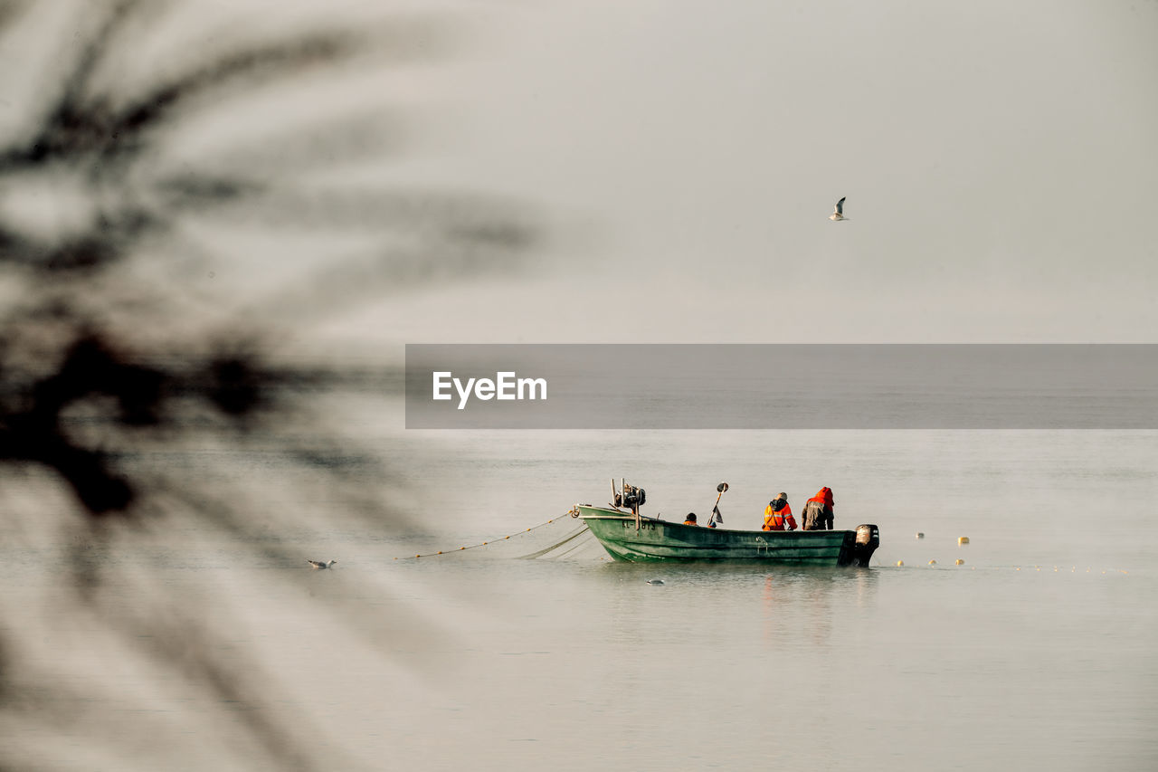 PEOPLE FISHING IN SEA AGAINST SKY