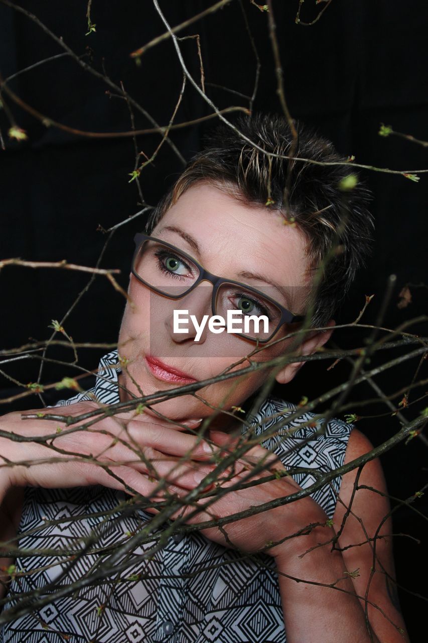 Close-up of thoughtful mature woman seen through twigs at night