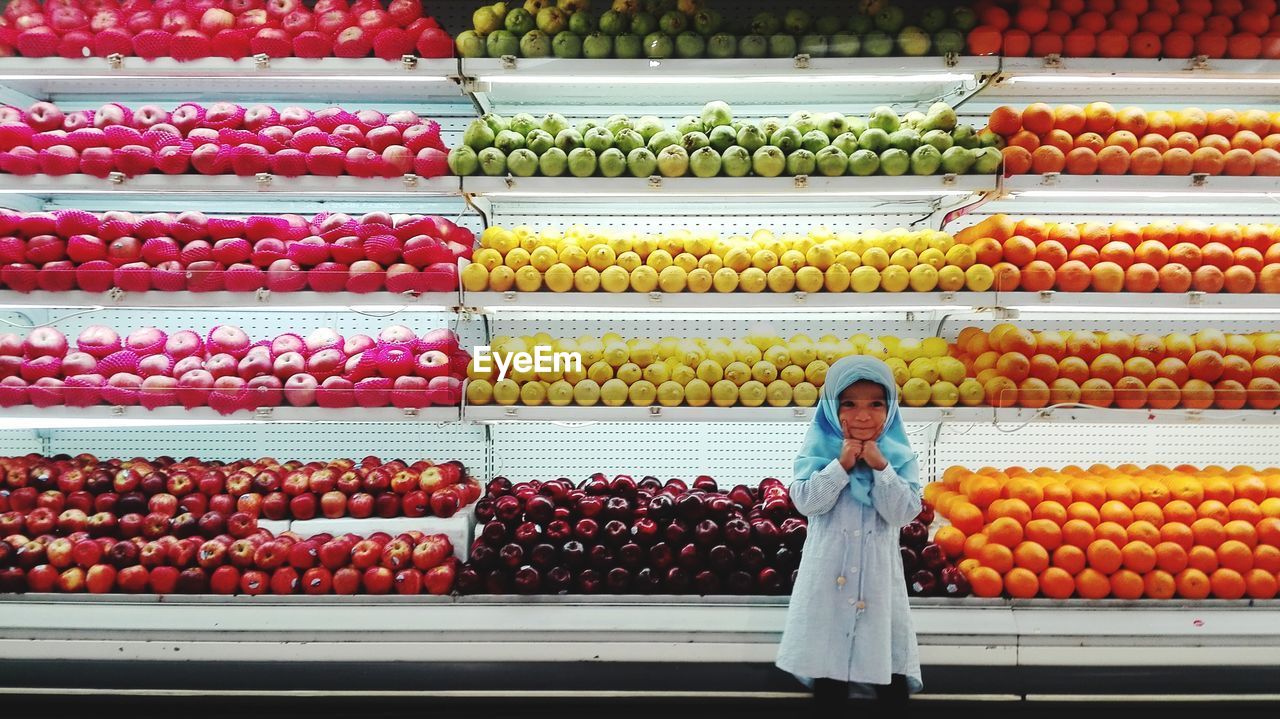 Portrait of cute girl wearing hijab standing against fruits in supermarket