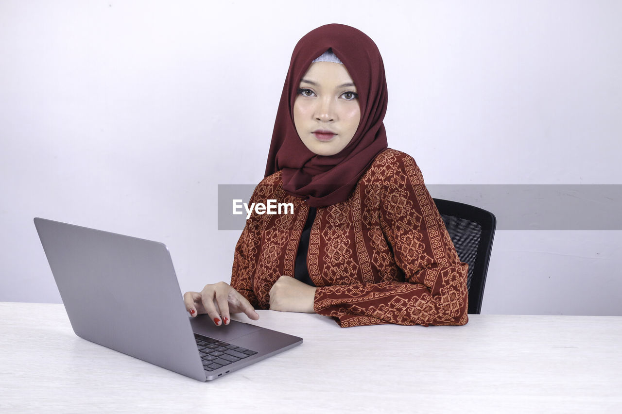 PORTRAIT OF YOUNG WOMAN USING SMART PHONE IN LAPTOP