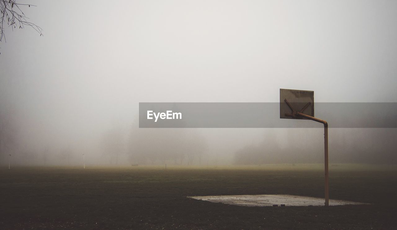 Basketball hoop on field against sky during foggy weather