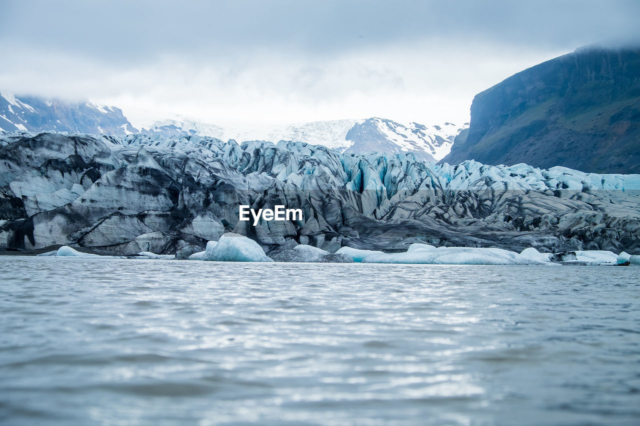 Scenic view of glaciers and mountains against cloudy sky