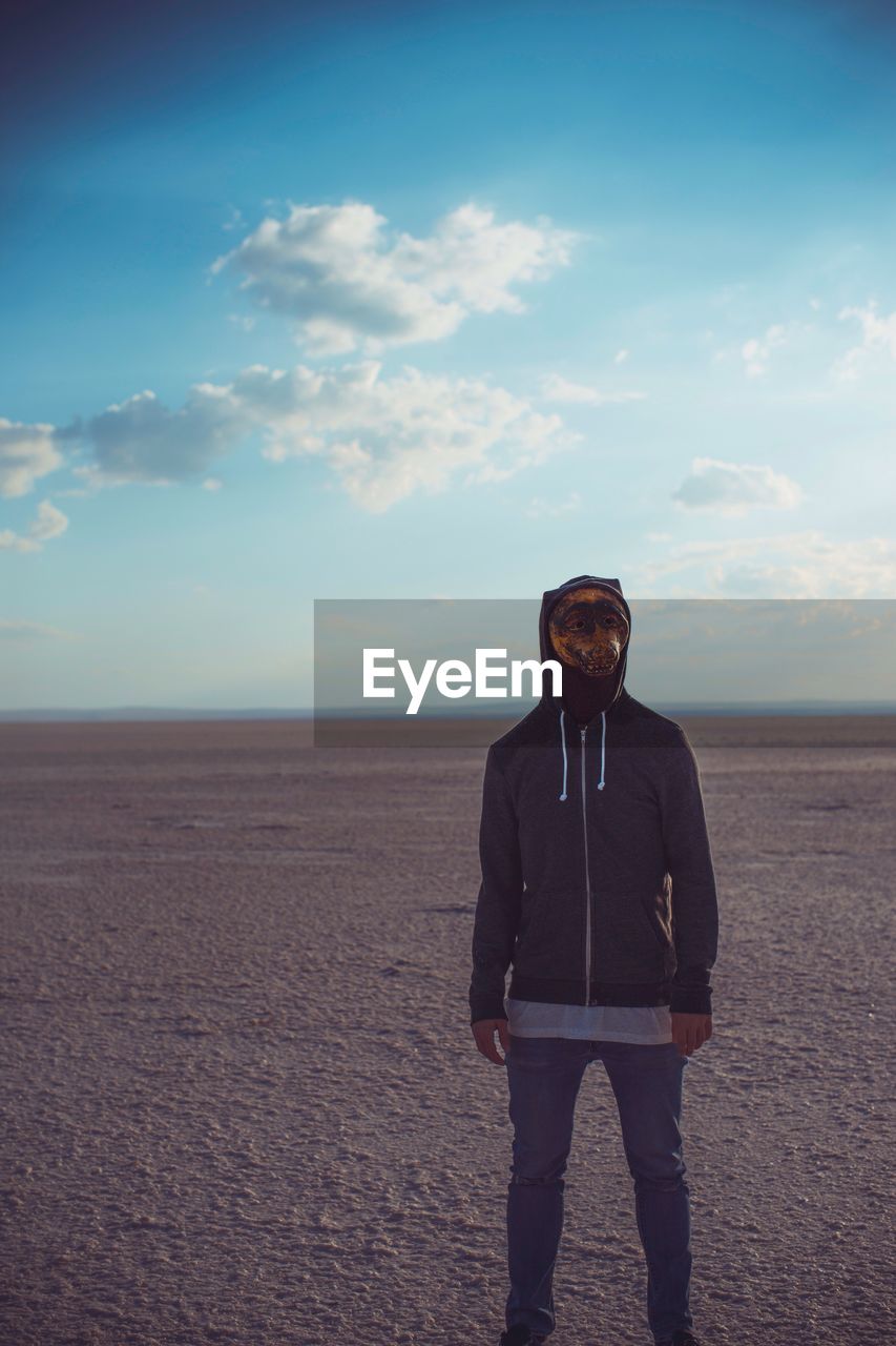 Man wearing mask while standing at beach against blue sky