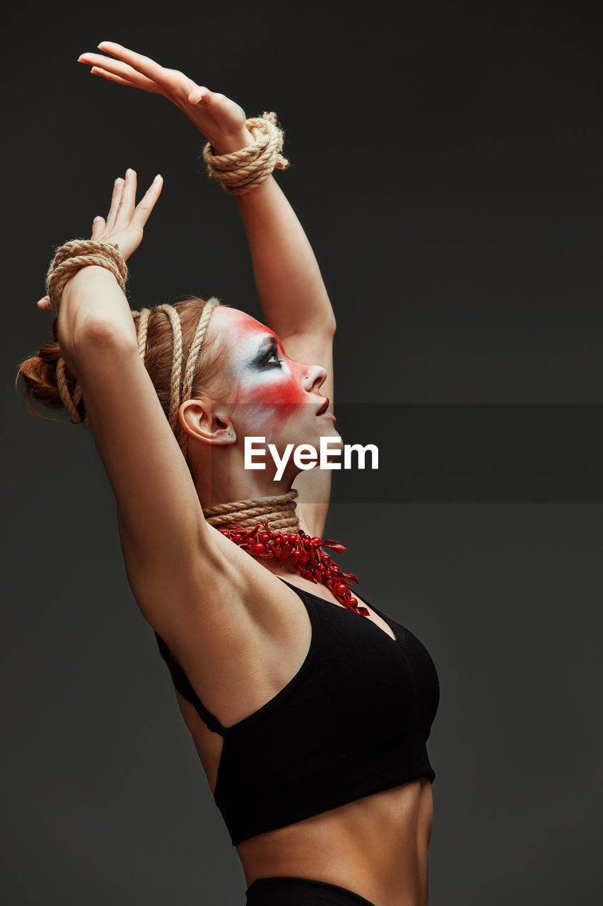 portrait of young woman with arms raised against black background