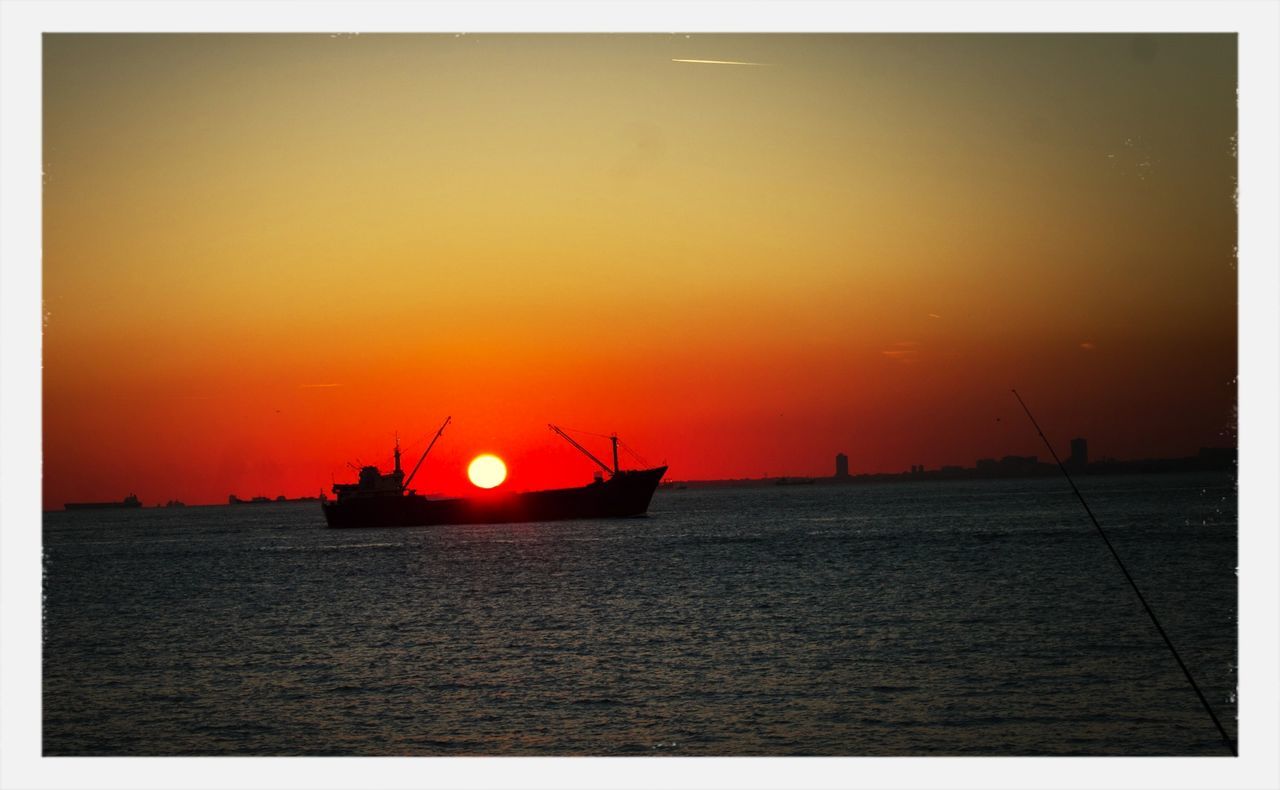 Silhouette of container ship in sea during sunset