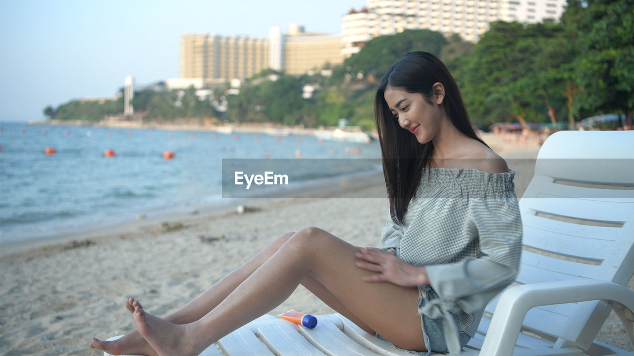 BEAUTIFUL YOUNG WOMAN SITTING ON BEACH