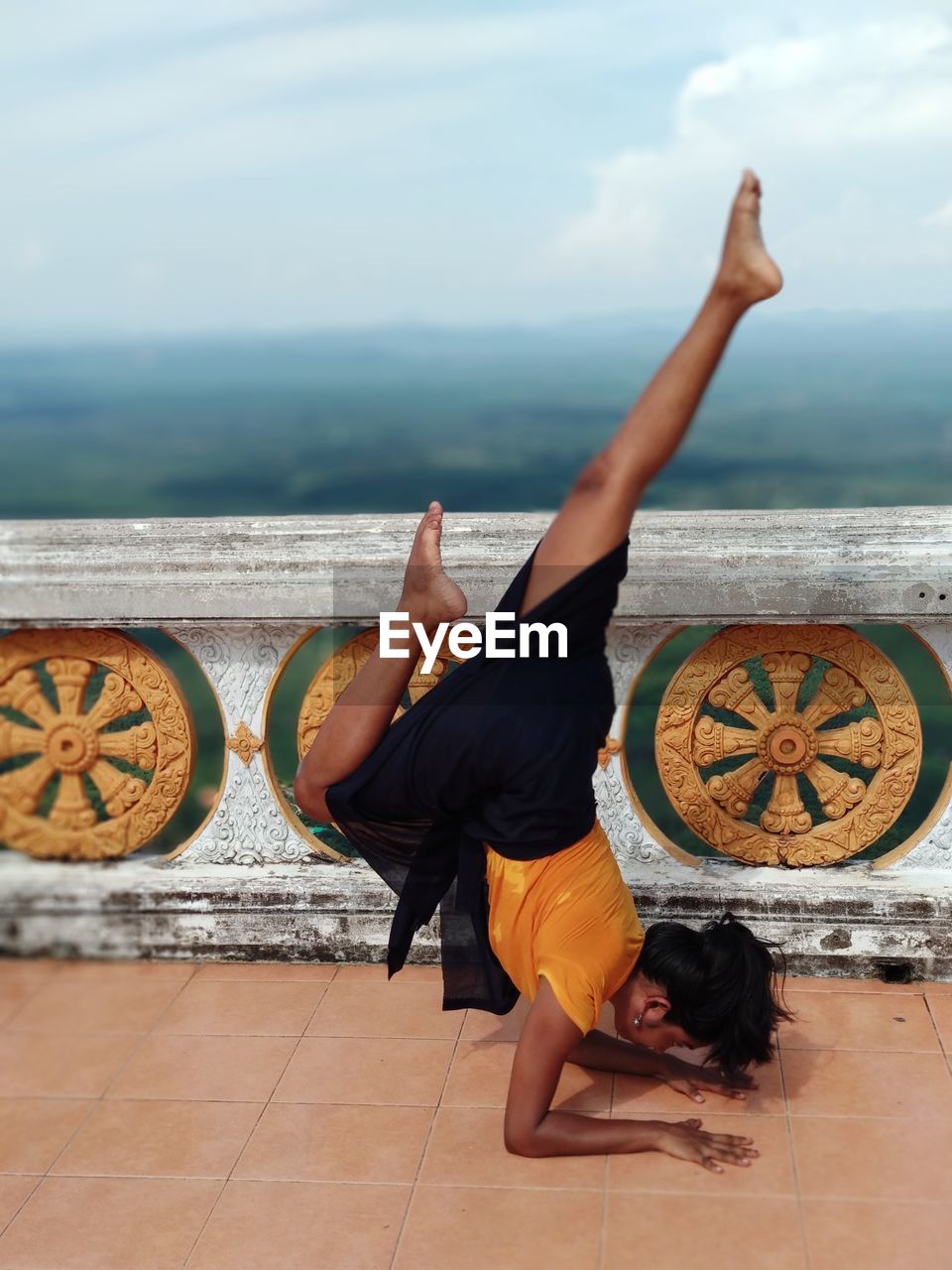 Woman doing handstand on building terrace against sky