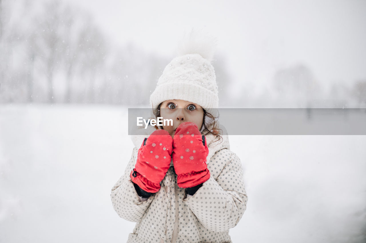 Portrait of young girl standing on snow covered field.