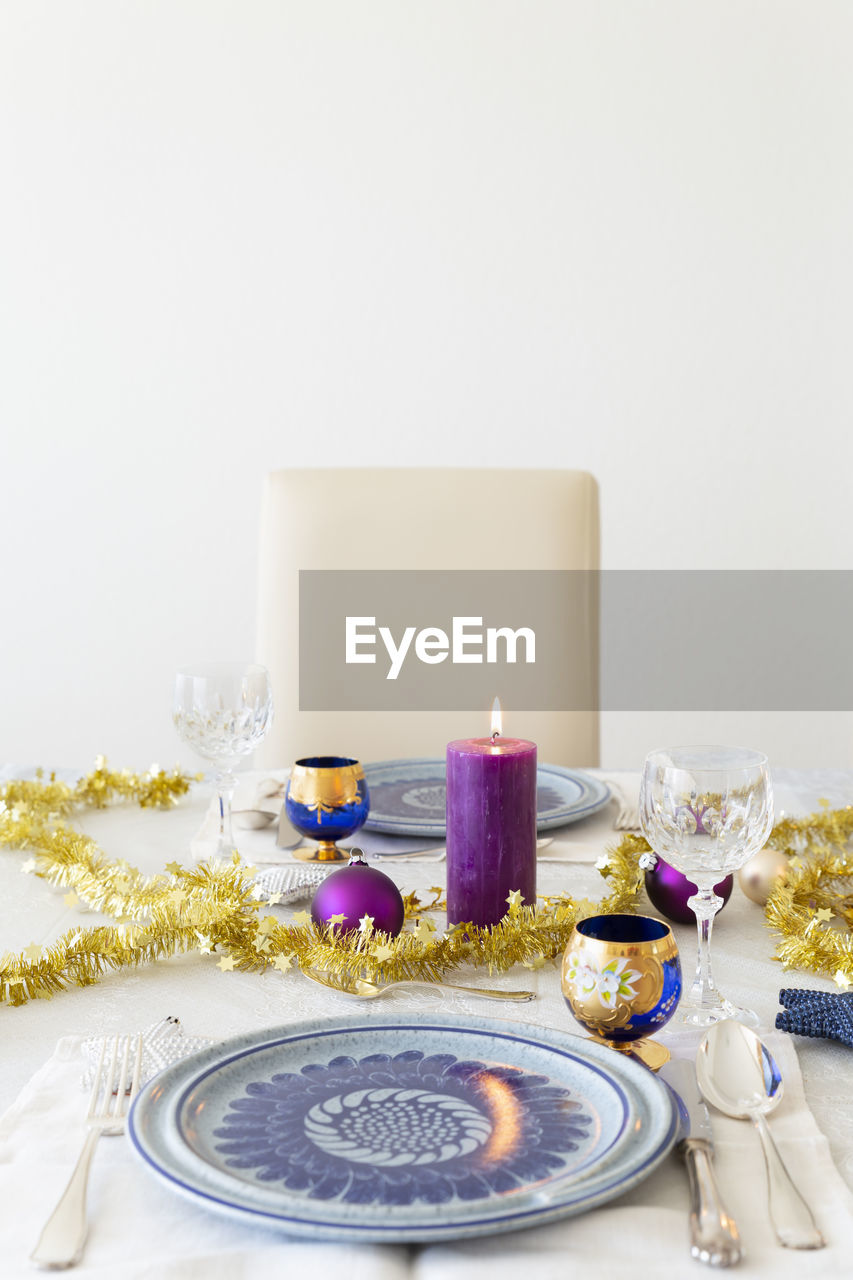 A decorated dining table with candles, cutlery, glasses, colorful christmas balls and gold tinsel