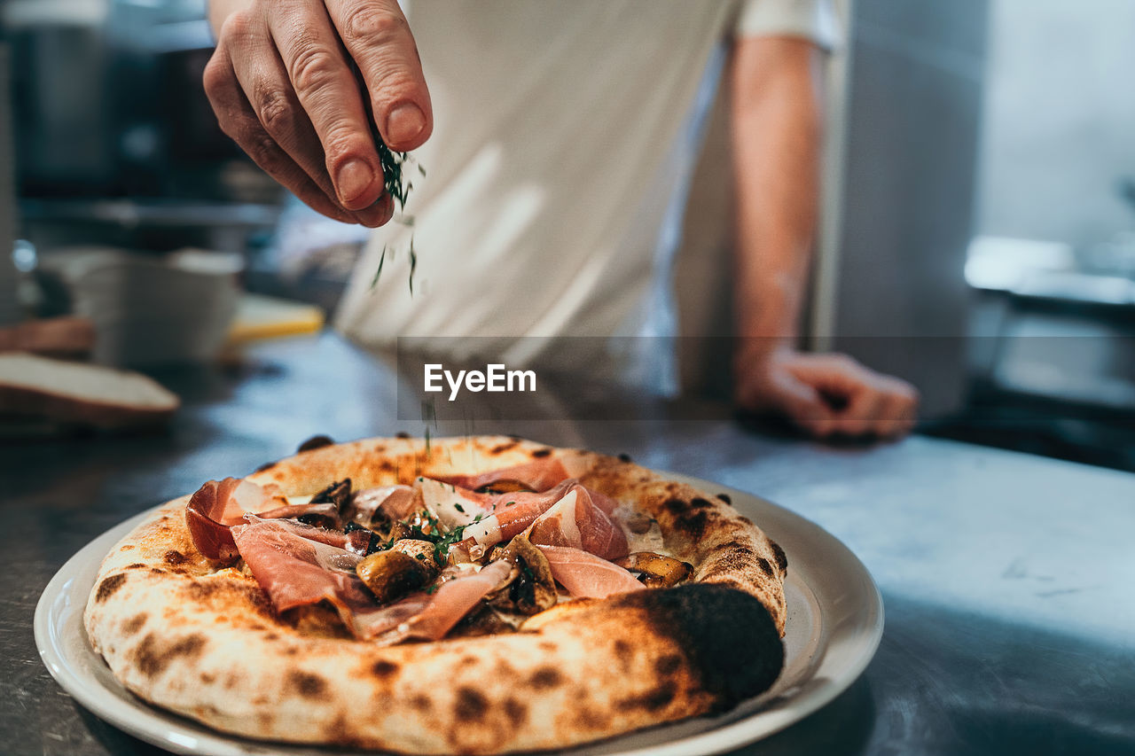 An italian chef garnishes the pizza just out of the stone oven.