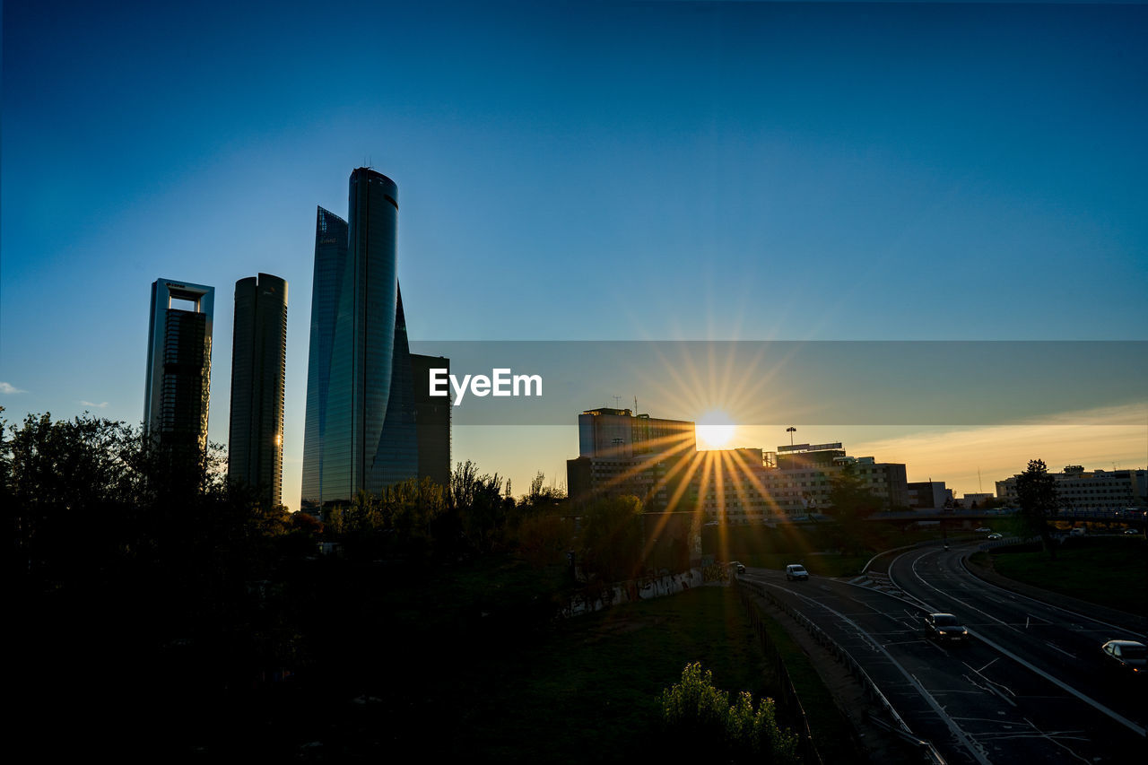 STREET AMIDST BUILDINGS AGAINST SKY DURING SUNSET