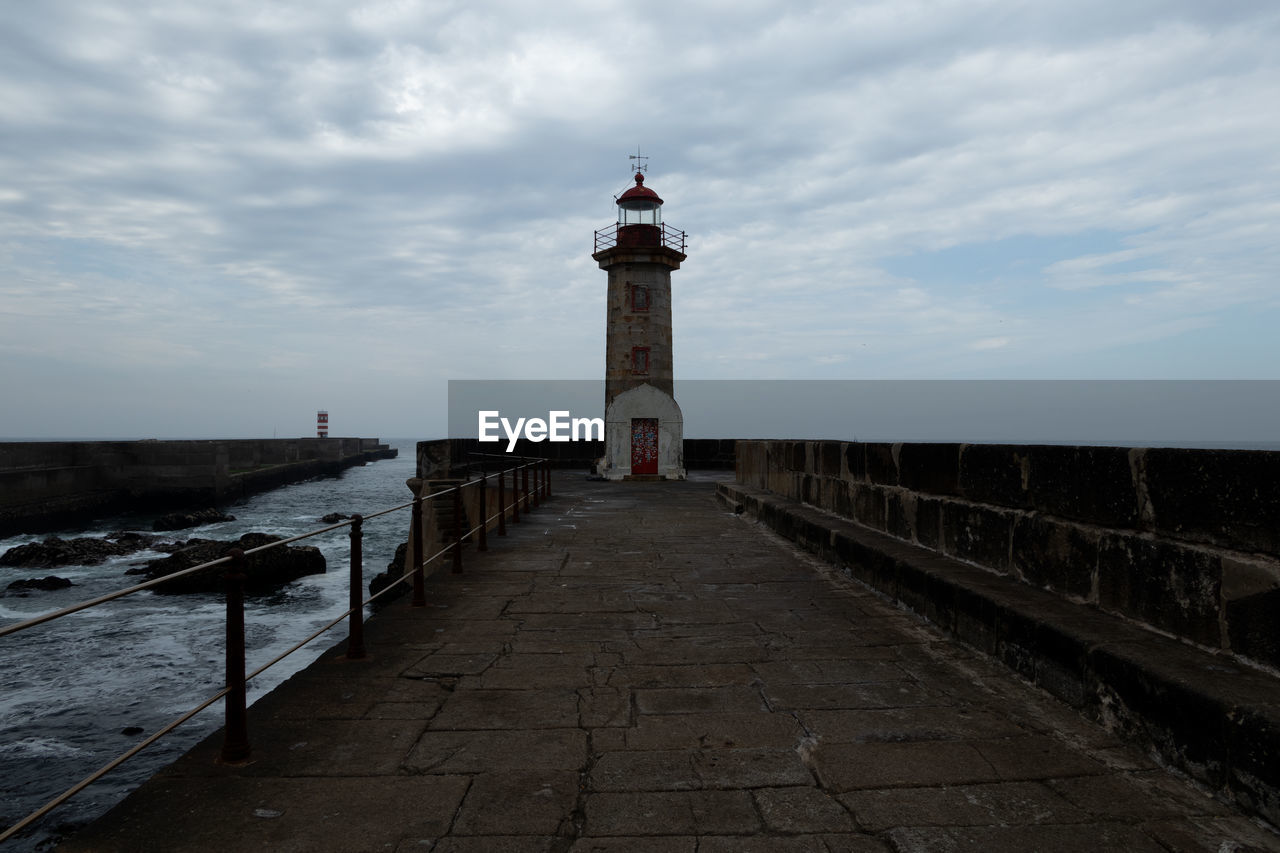 LIGHTHOUSE AMIDST BUILDINGS AGAINST SKY