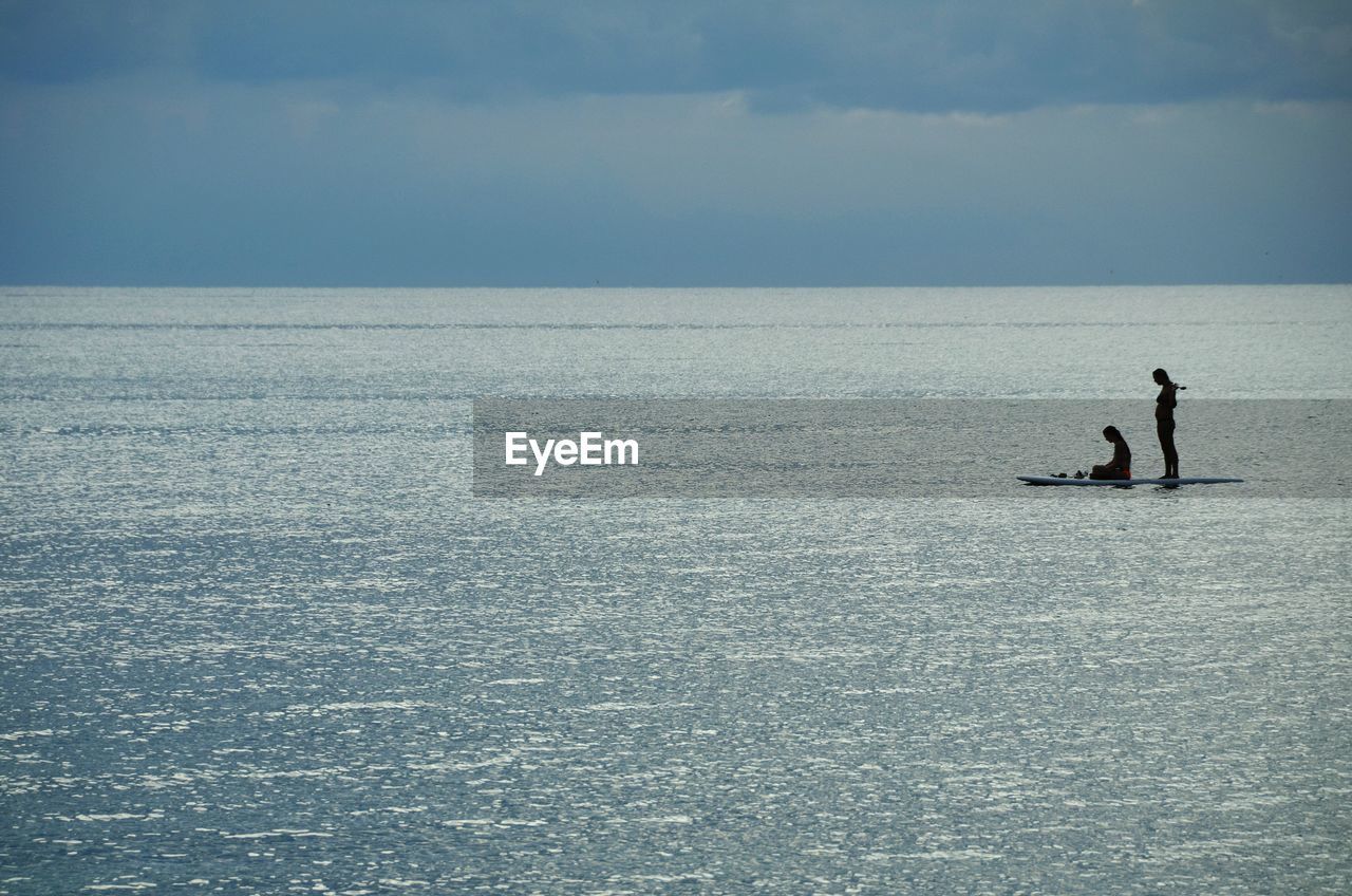 Women paddleboarding in sea against sky