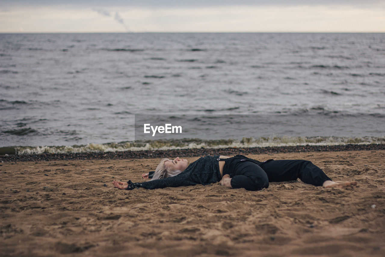 Young woman relaxing on sand at beach against sky