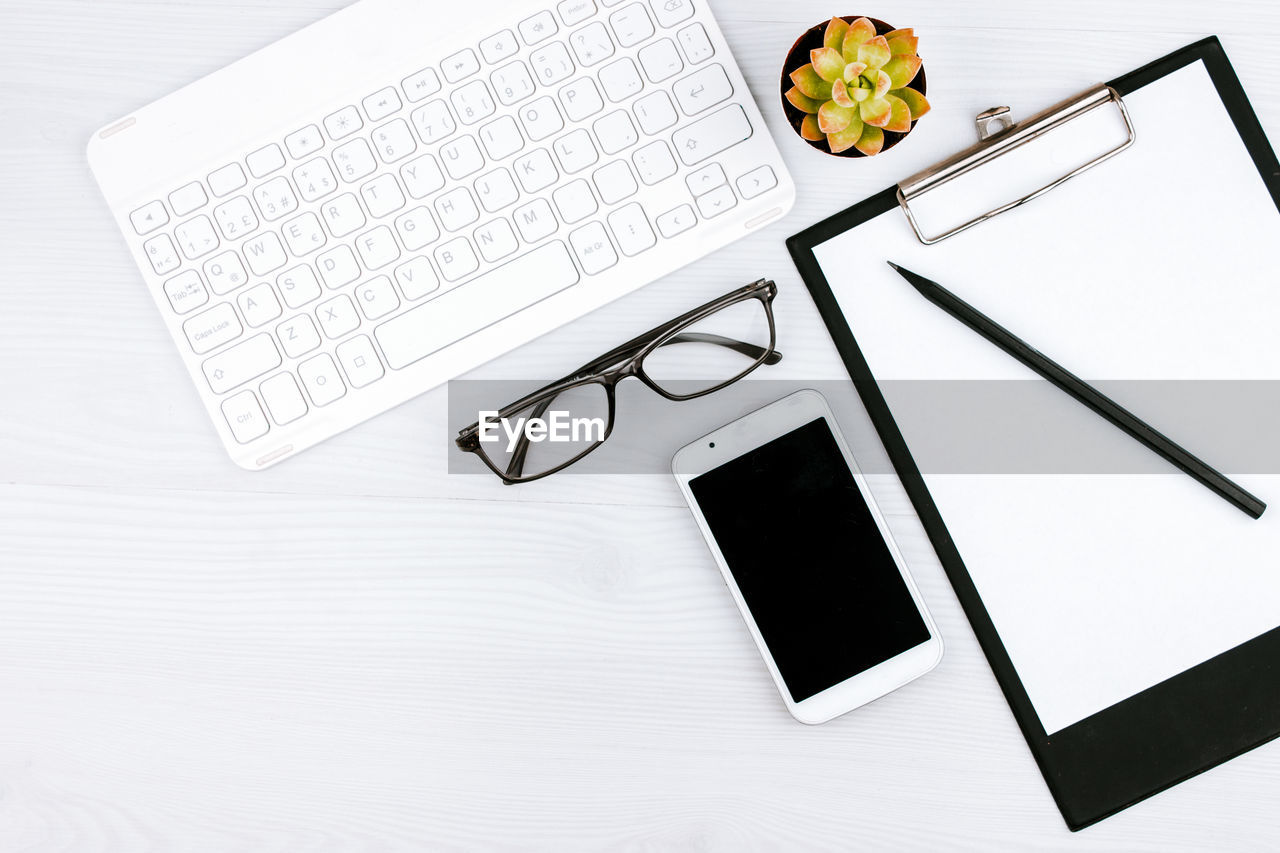 Business concept. work from home. office flatlay with white keyboard, reading glasses and notebook.