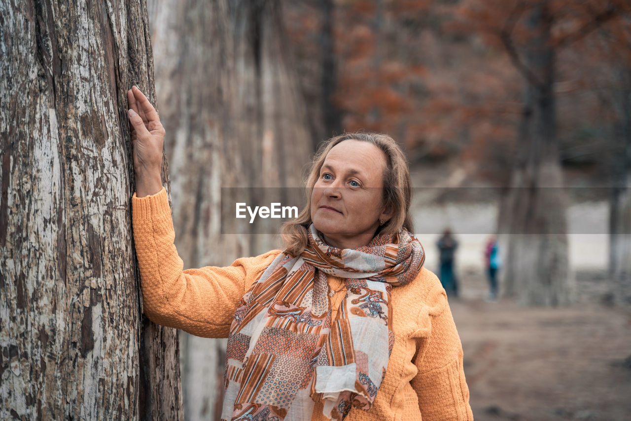 Portrait of woman standing by tree trunk