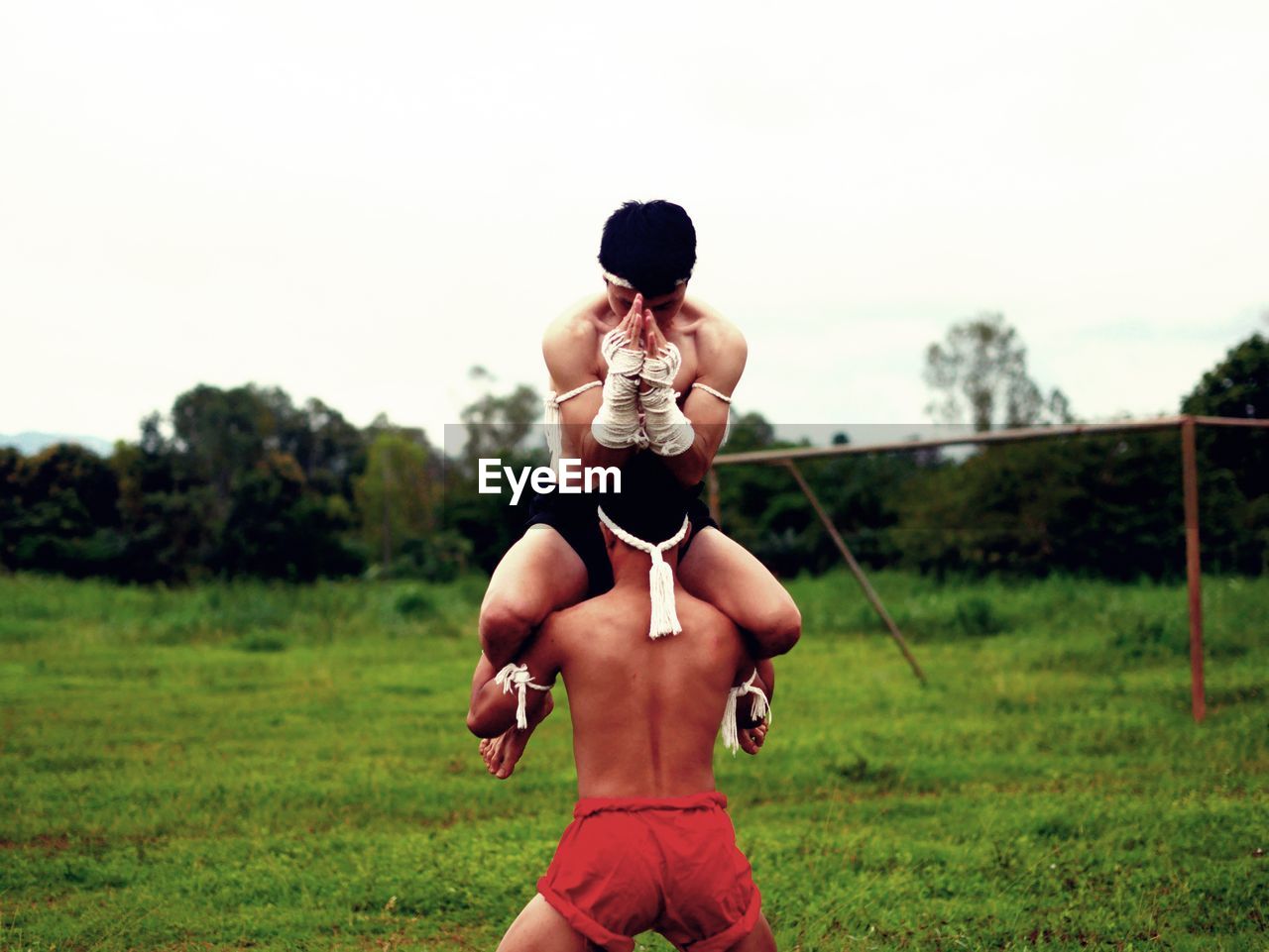 Shirtless male fighters practicing on grass against sky