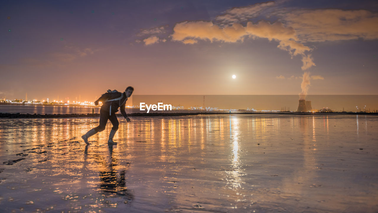 Man standing at beach against sky at dusk