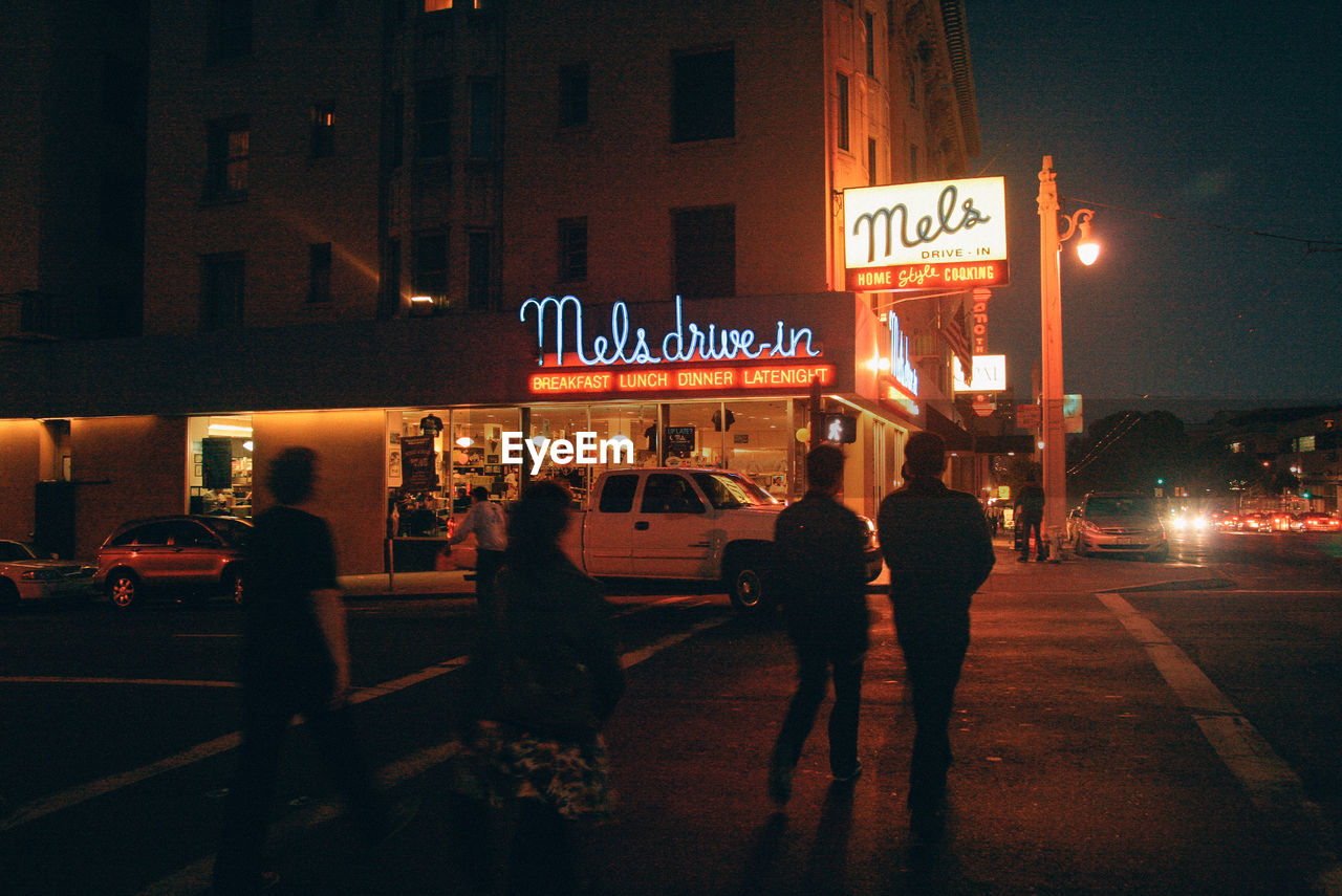 PEOPLE WALKING ON ILLUMINATED STREET AT NIGHT