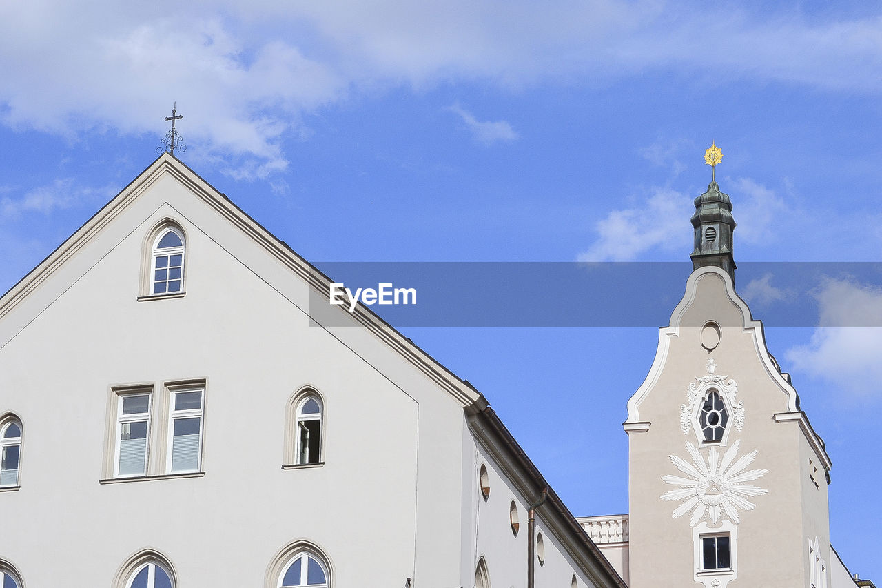 Low angle view of cross amidst buildings against sky